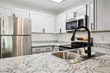 A kitchen with a stainless steel refrigerator, microwave, and a granite countertop.